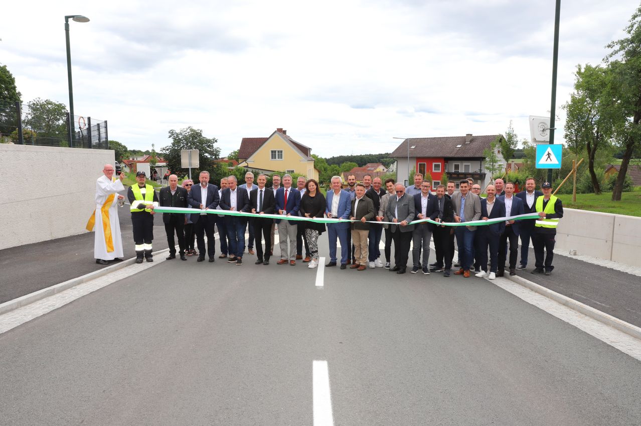 Eine Gruppe von Menschen steht in einer Reihe und hält eine lange grüne Schleife, wahrscheinlich zur Feier eines Ereignisses auf der Straße.