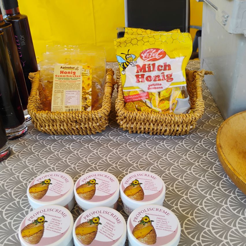 Two wicker baskets on a table display honey products. One basket contains a bag of honey candies and the other has a jar of propolis cream.