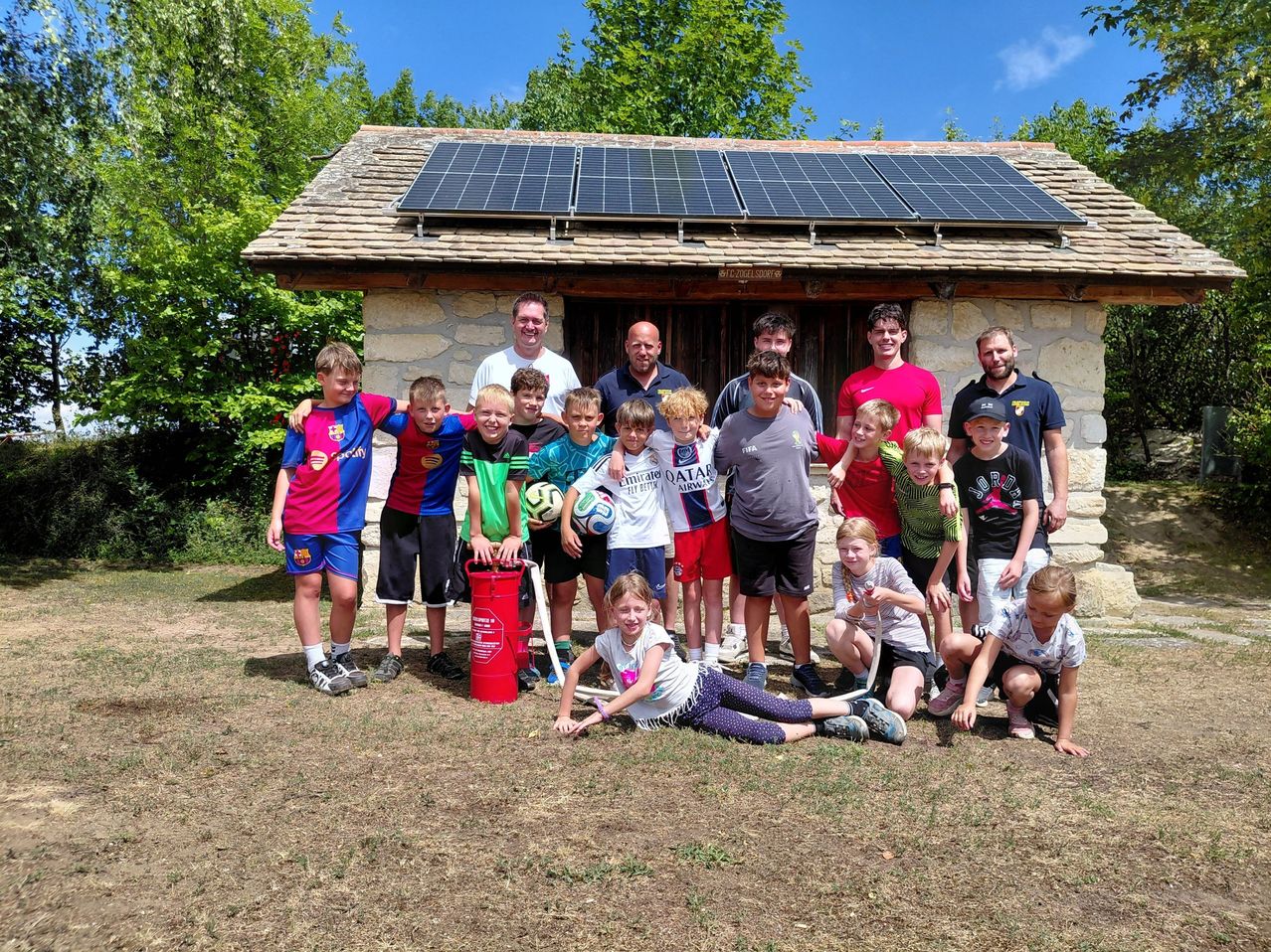 Eine Gruppe von Kindern und Erwachsenen posiert vor einem kleinen Gebäude mit Solarmodulen auf dem Dach.