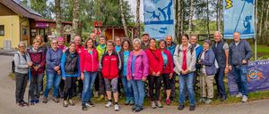 Eine Gruppe von Menschen in Wanderausrüstung steht vor einem Birkenwald, zwei Banner stehen dahinter.