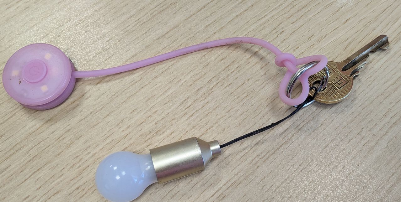 Eine kleine rosa Glühbirne mit einem silbernen Metallgehäuse und einem schwarzen Kabel, befestigt an einem rosa Griff mit einem silbernen Ring.