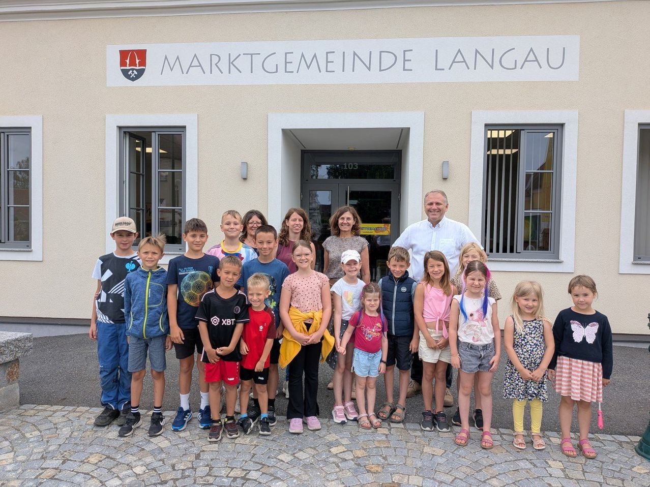 Eine Gruppe von Kindern und Erwachsenen posiert für ein Foto vor einem Gebäude mit der Aufschrift Marktgemeinde Langau.