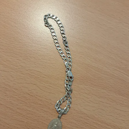 Eine silberne Kette mit einem Anhänger, der eine religiöse Figur darstellt, liegt auf einer Holzoberfläche.
