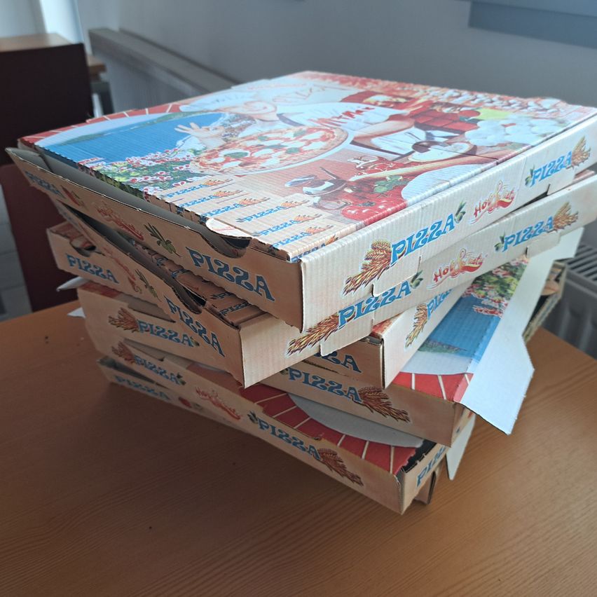 Ein Stapel Pizzakartons mit bunten Illustrationen, auf einem Holztisch gestapelt. Jeder Karton zeigt ein anderes Pizzadesign.