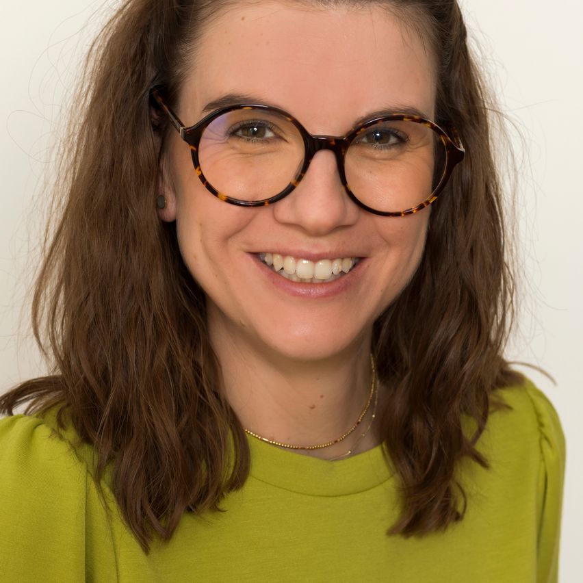 Eine lächelnde Frau mit braunen Haaren, die eine Brille und ein grünes Hemd trägt. Sie schaut direkt in die Kamera.
