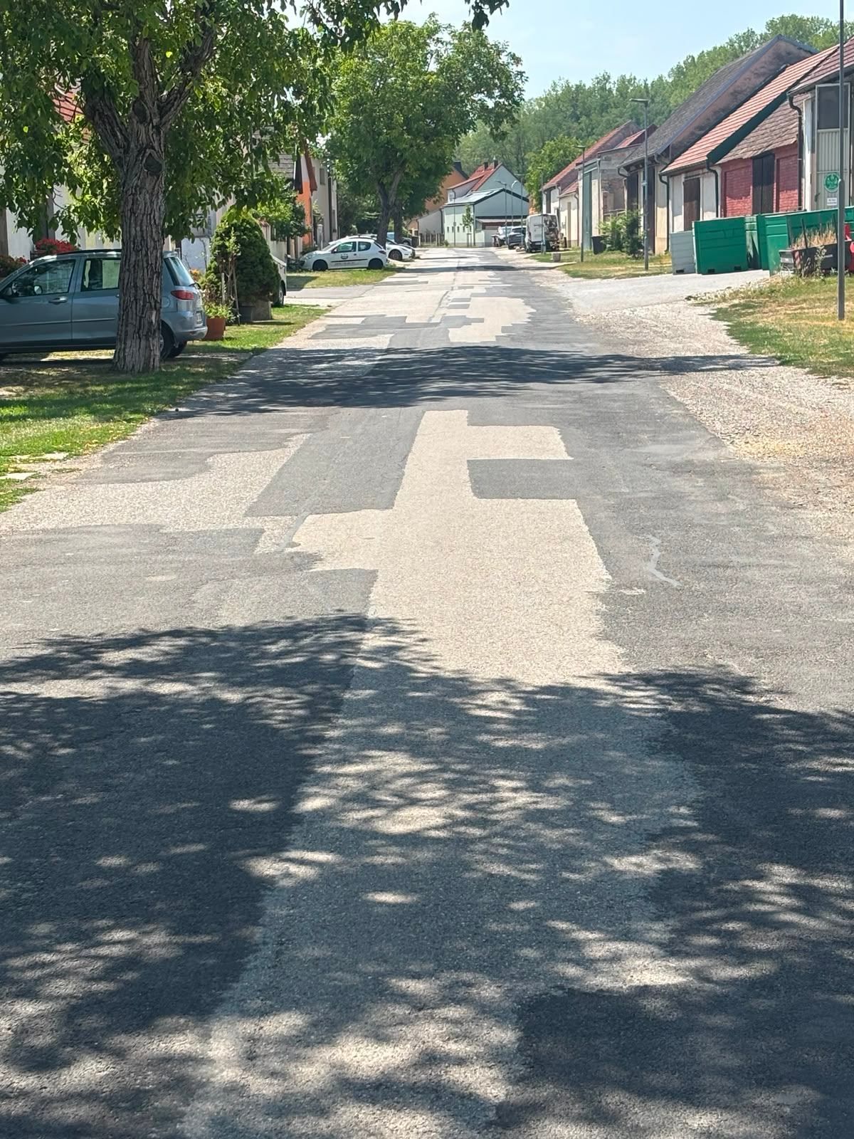 Eine ruhige Straße mit geparkten Autos und Bäumen an einem sonnigen Tag. Die Straße ist aus Kies.