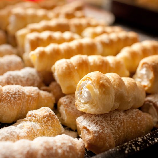 Ein Tablett mit Croissants gefüllt mit Sahne und bestäubt mit Puderzucker. Einige sind spiralförmig, andere einfach. Sie sind frisch und warm.