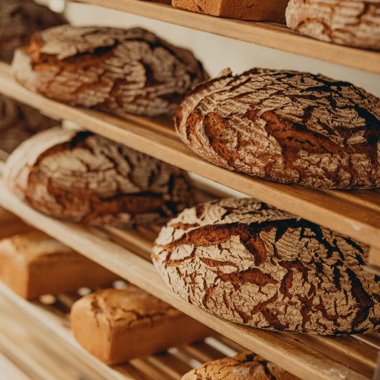 Ein Holzregal mit mehreren Lagen von Artisan-Brot gefüllt, jedes mit unterschiedlichen Texturen und Krusten. Das Brot ist in Reihen auf dem Regal angeordnet.