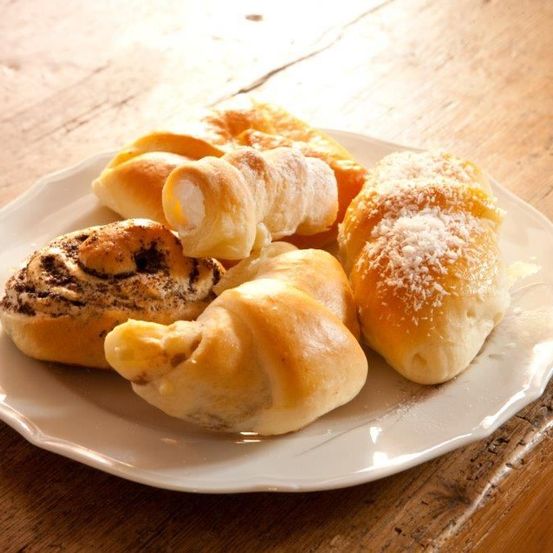 Ein Teller mit Gebäck, darunter Croissants, dänisches Gebäck und Brot mit Belägen, steht auf einem Holztisch.