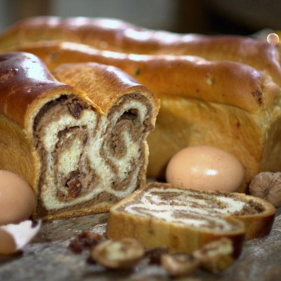 Eine Nahaufnahme von geschnittenem Schokoladen- und Rosinenbrot mit zwei Eiern und Nüssen im Vordergrund.
