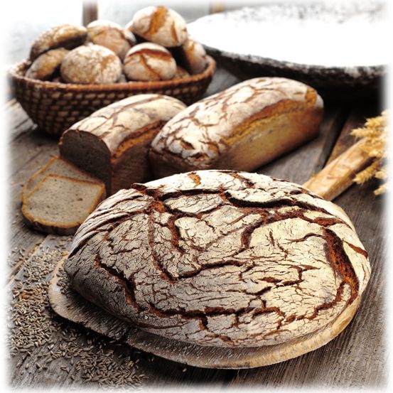 Auf einem Holztisch sind verschiedene Brote und Brötchen zu sehen. Zwei Brote sind ganz und eines ist geschnitten. Es gibt auch einen Korb mit Brötchen.