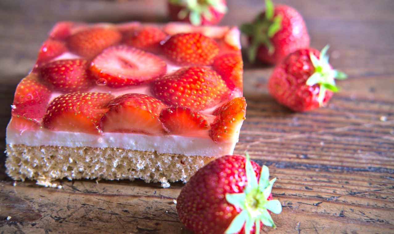 Eine Nahaufnahme eines mit Erdbeeren garnierten Desserts auf einer Holzoberfläche mit ganzen Erdbeeren im Hintergrund.