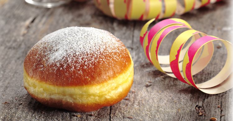 A powdered sugar-dusted doughnut rests on a wooden surface, with colorful paper streamers in the background.