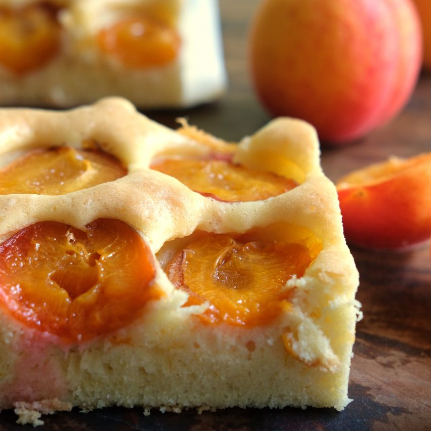 A close-up of a slice of apricot tart with golden-brown crust and juicy apricot slices on a wooden surface.