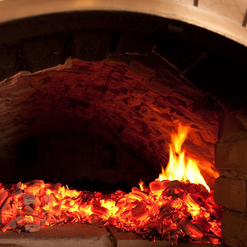 A close-up view of a wood-burning oven with glowing coals inside, casting a warm, reddish light.