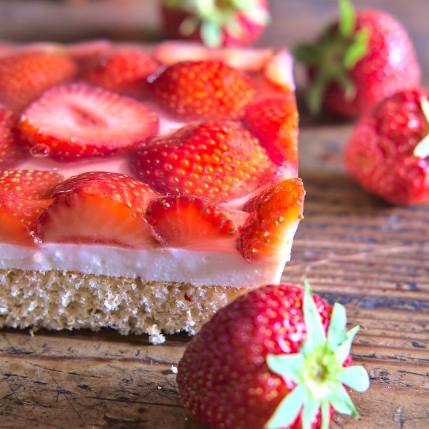 Ein Nahaufnahme eines Desserts mit einer Kruste, geschichtet mit Erdbeeren und weißer Creme, auf einer Holzoberfläche.