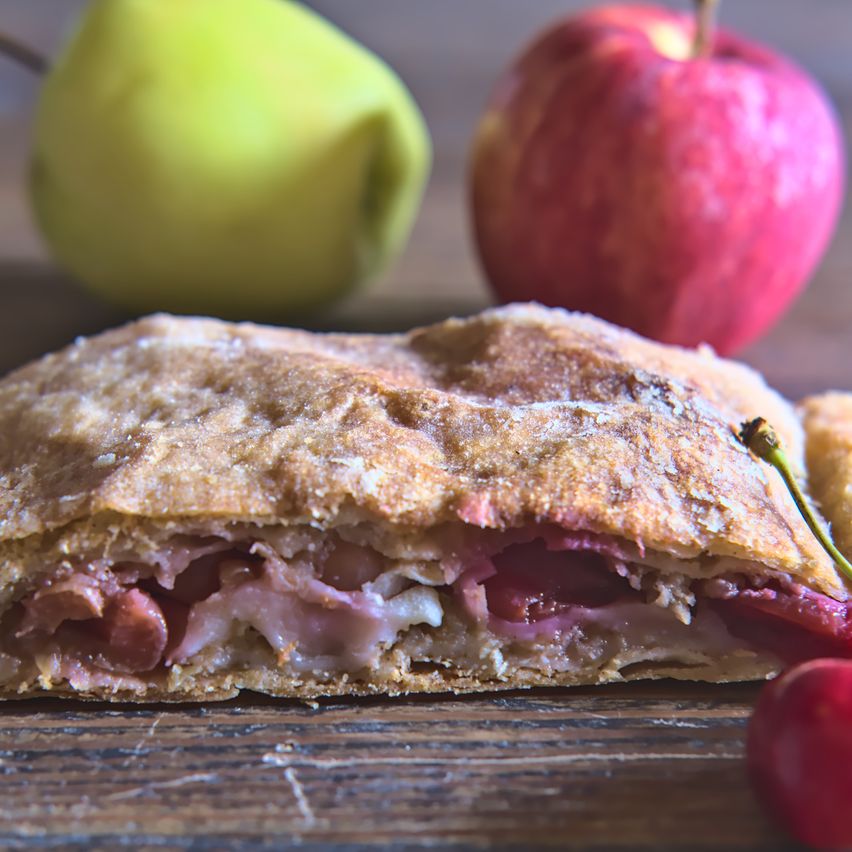 Nahaufnahme eines geschnittenen Sandwiches auf einer Holzoberfläche mit einer Birne und einem Apfel im Hintergrund.
