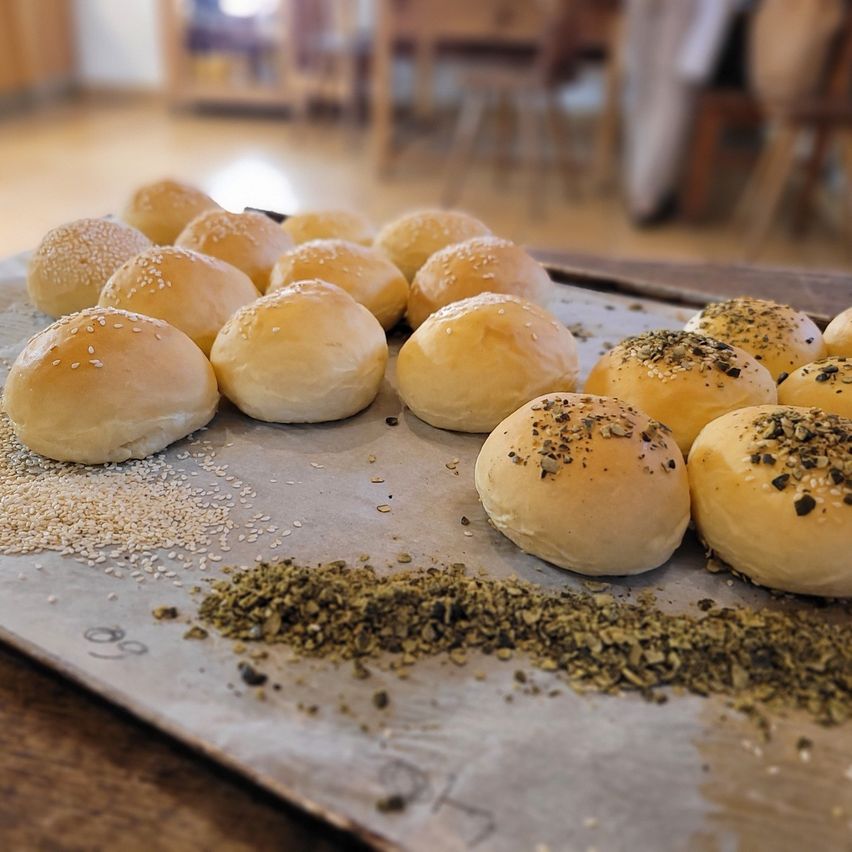 A tray of bread rolls on a kitchen counter, some topped with sesame seeds, others with herbs, and a sprinkling of herbs on the tray.