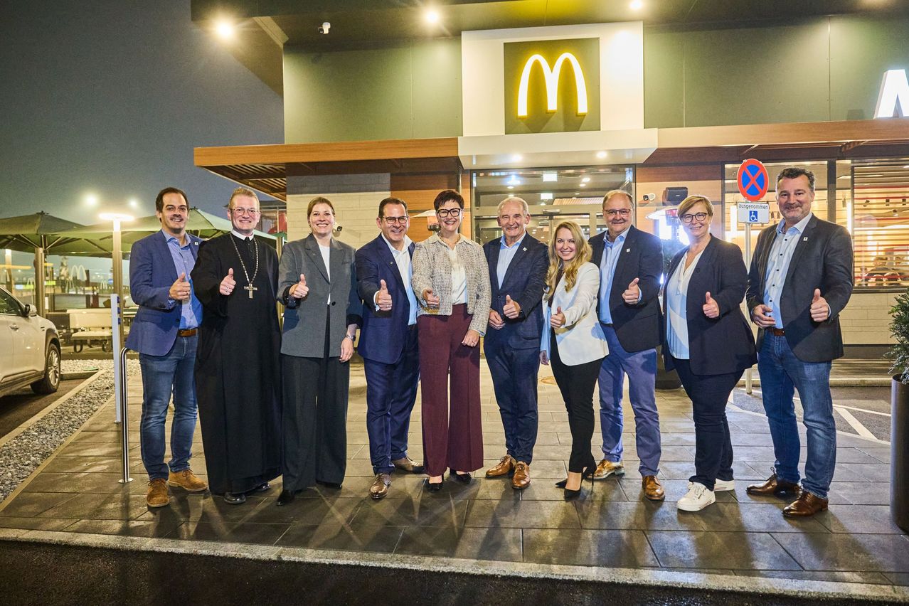 Eine Gruppe von Menschen steht nachts vor einem McDonald's-Restaurant, alle lächeln und geben Daumen hoch.