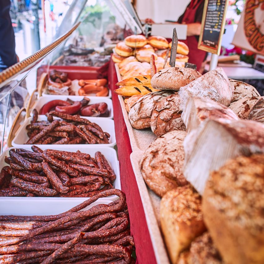 Ein Lebensmittelstand mit einer Vielzahl von Fleisch- und Brotsorten auf Tabletts. Zu den Fleischsorten gehören Würste und Salami. Zu den Brotsorten gehören Baguettes und andere Laibe.