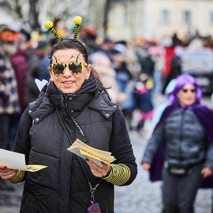 Eine Frau, verkleidet als Biene, trägt bienenthematische Sonnenbrillen und liest ein Stück Papier, während sie sich unter einer Menge auf einem Festival bewegt.