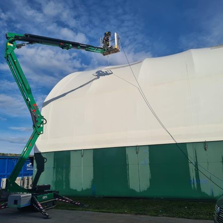 Ein grüner Kran wird verwendet, um das weiße Dach eines Gebäudes unter blauem Himmel zu streichen.