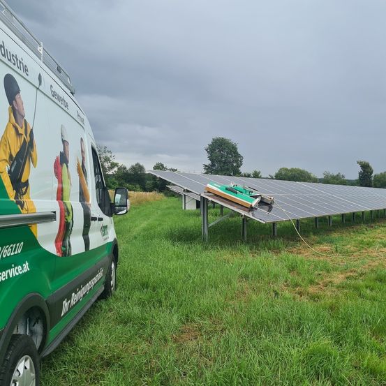 Ein Van mit Reinigungsgeräten steht neben einer Solarpanel-Anlage auf einem Rasenfeld. Der Himmel ist bewölkt.