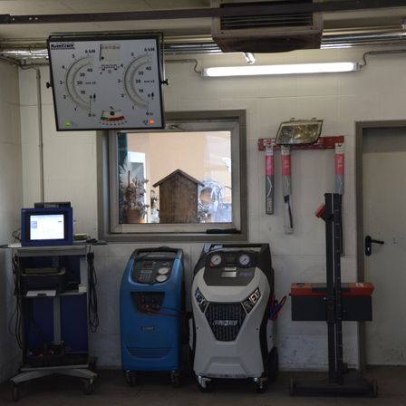 Ein Werkstattraum enthält einen Monitor, eine Waage und zwei Maschinen. Ein Fenster befindet sich an der Wand. Ein Werkzeug ist neben einer Tür an der Wand montiert.