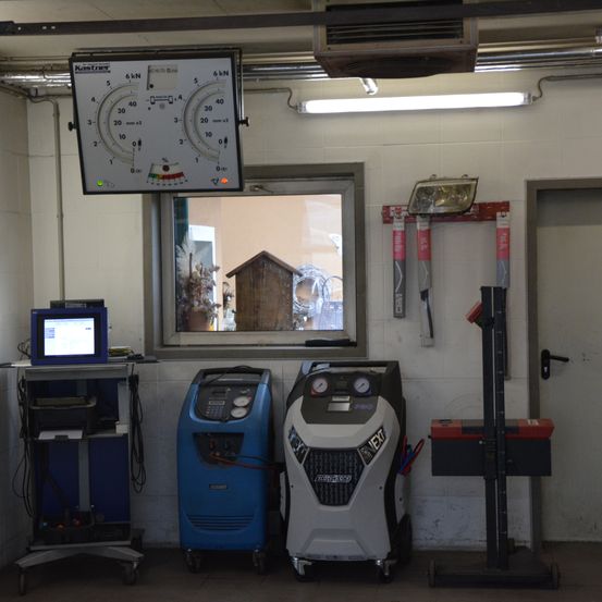 Ein Werkstattraum enthält einen Monitor, eine Waage und zwei Maschinen. Ein Fenster befindet sich an der Wand. Ein Werkzeug ist neben einer Tür an der Wand montiert.