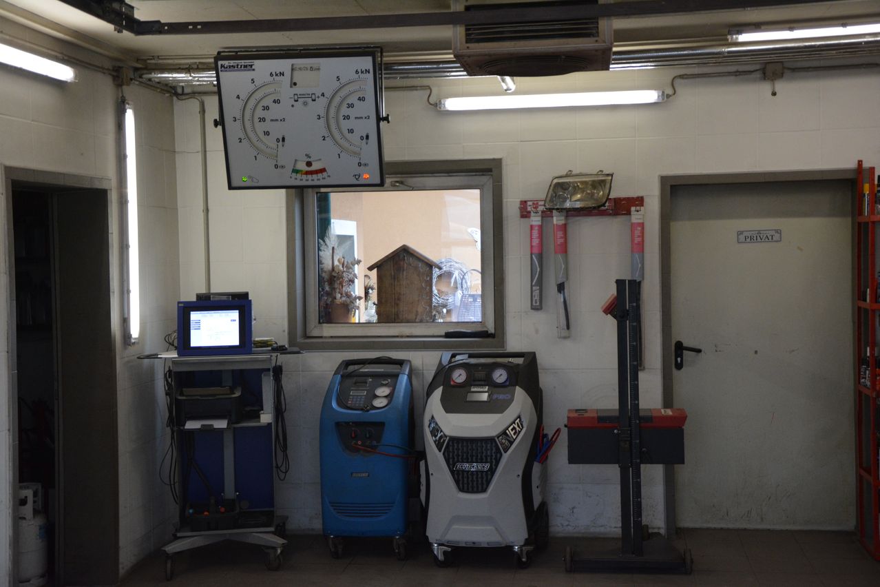 Ein Werkstattraum enthält einen Monitor, eine Waage und zwei Maschinen. Ein Fenster befindet sich an der Wand. Ein Werkzeug ist neben einer Tür an der Wand montiert.