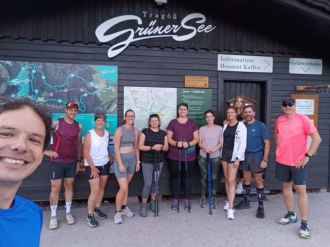 A group of people in athletic wear pose for a photo in front of a building with a sign that reads 'Grüner See'.