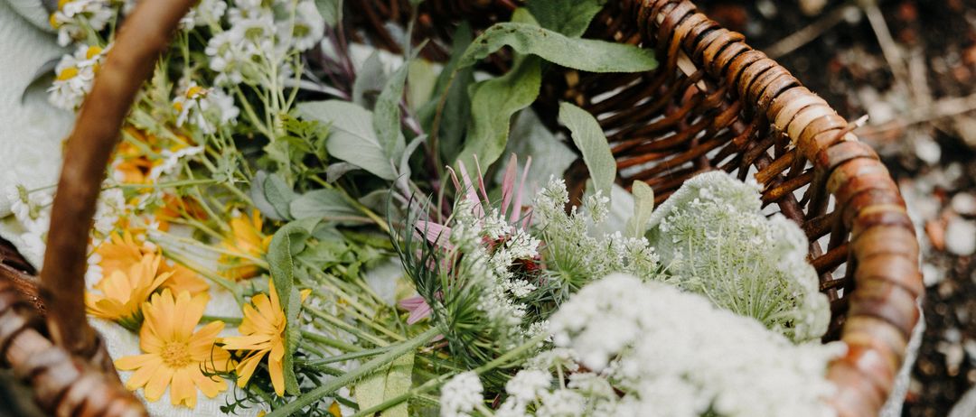 Ein Korb aus Weide gefüllt mit einer Vielfalt von Blumen, darunter weisse, gelbe und grüne, auf einem weissen Tuch.