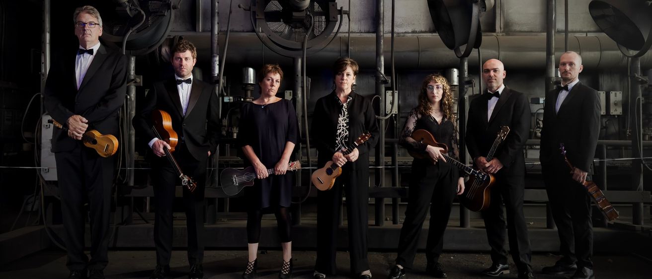 Eine Gruppe von Musikern in Anzug und Abendkleid posiert mit Gitarren in einer industriellen Umgebung.