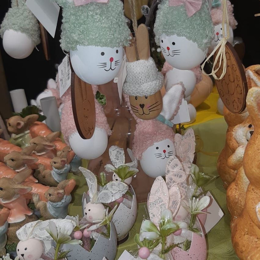 Eine Sammlung von Osterfiguren in verschiedenen Designs. Einige haben rosa Schleifen und Mützen, andere haben weiße und grüne Mützen. Sie sind auf einer grünen Oberfläche mit einigen Blumen und Blättern angeordnet.