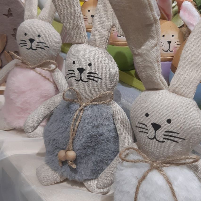 Vier gehäkelte Hasenfiguren sitzen auf einer weißen Oberfläche. Sie haben Jutesäcke als Körper und Plüschohren. Jede Figur hat eine einzigartige Farbe und einen dekorativen Band.