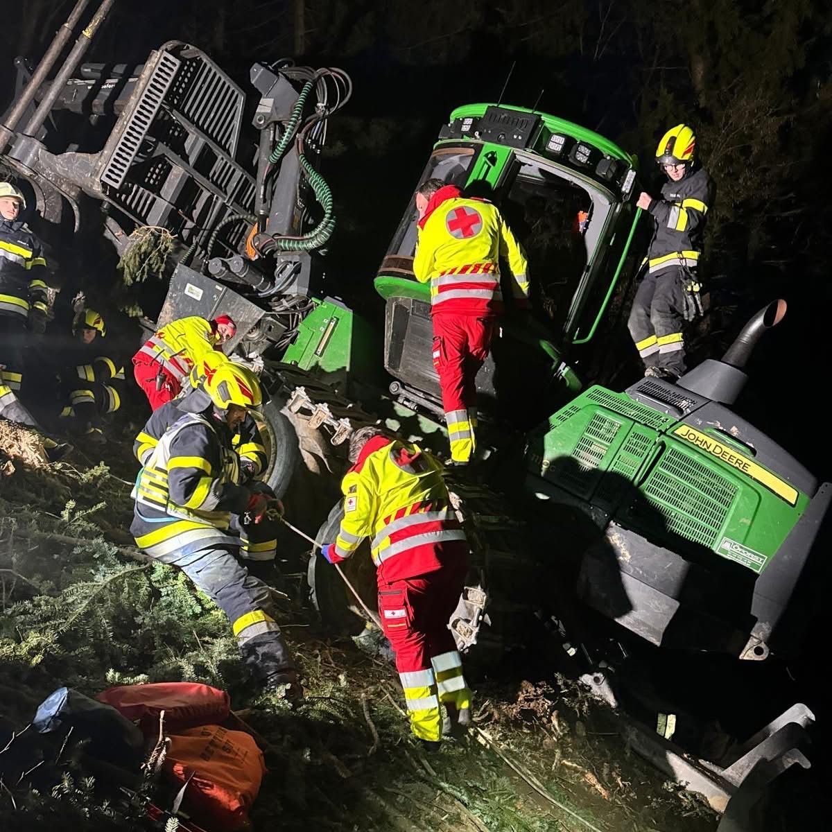 Einsatzkräfte in gelben und roten Uniformen kümmern sich um ein umgekipptes John Deere-Fahrzeug in einem Wald. Ein Helfer hält ein Seil, während andere in das Fahrzeug klettern.