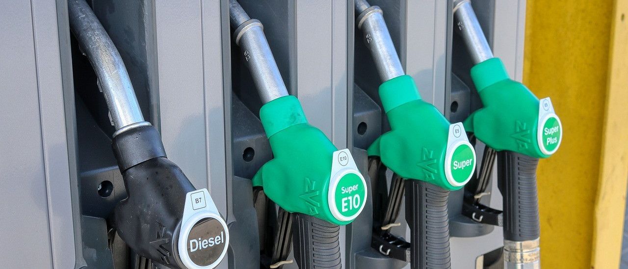 Vier Zapfsäulen mit Düsen sind aufgereiht. Die linke Düse ist schwarz und sagt Diesel. Die nächste ist grün und sagt Super E10. Die folgende sagt Super E5. Die letzte ist grün und hat ein grünes Etikett mit dem Wort Super.