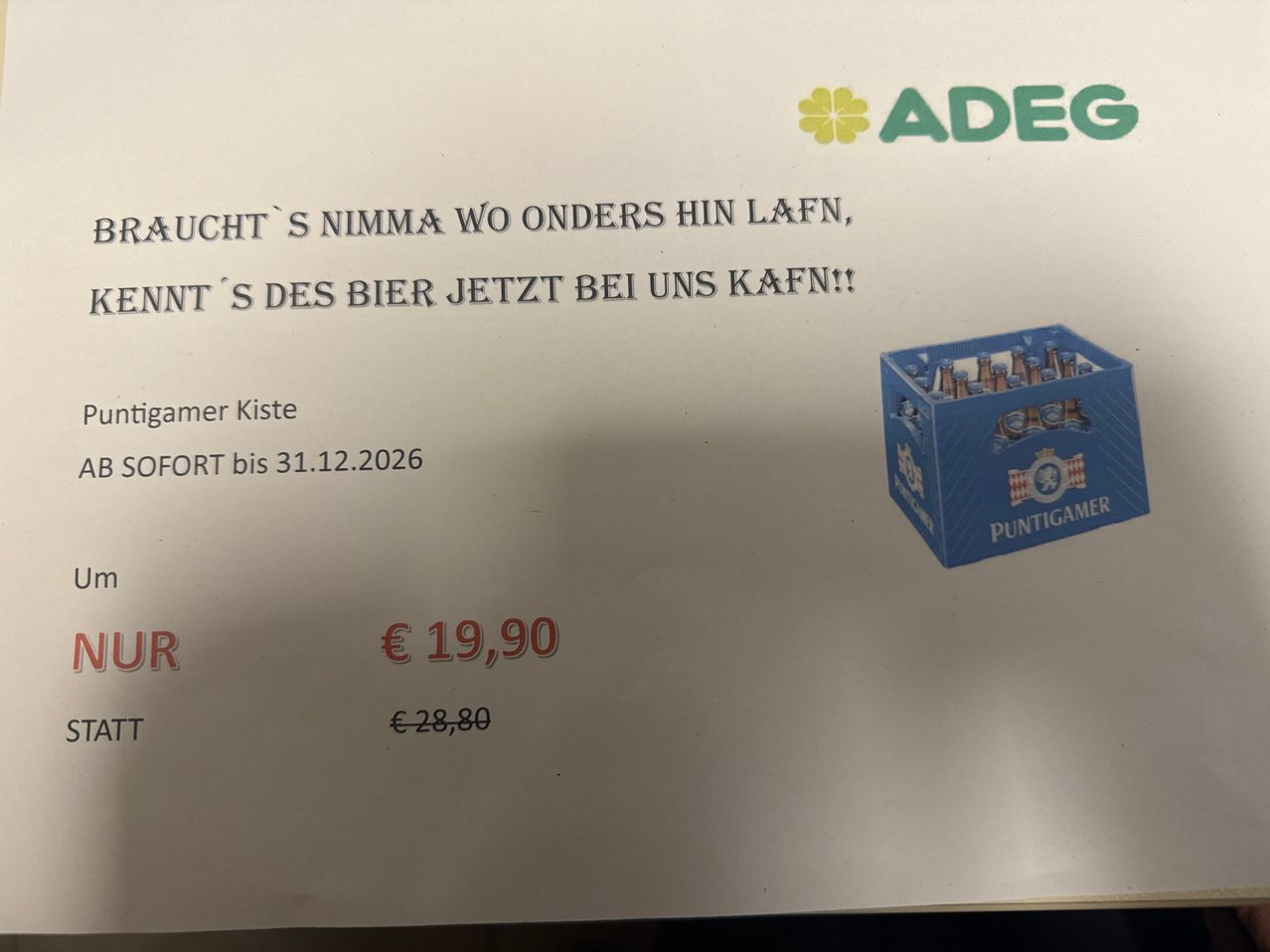Das Bild zeigt eine blaue Box mit der Aufschrift 'PUNTIGAMER'. Unter der Box befindet sich ein Preisschild. Der Text über der Box lautet 'AUCHT`S NIMMA WO ONDERS HIN LAFN, NT S DES BIER JEZT BEI UNS KAFN!!'. Darunter steht ein Datum 'FORT bis 31.12.2026'. Der Preis der Box ist als €19,90 und €28,80 ausgewiesen.