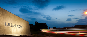 Ein Werbeschild ist in der Dämmerung beleuchtet, der Himmel ist blau mit einigen Wolken, und Autos erzeugen lange Lichtspuren auf der Straße.