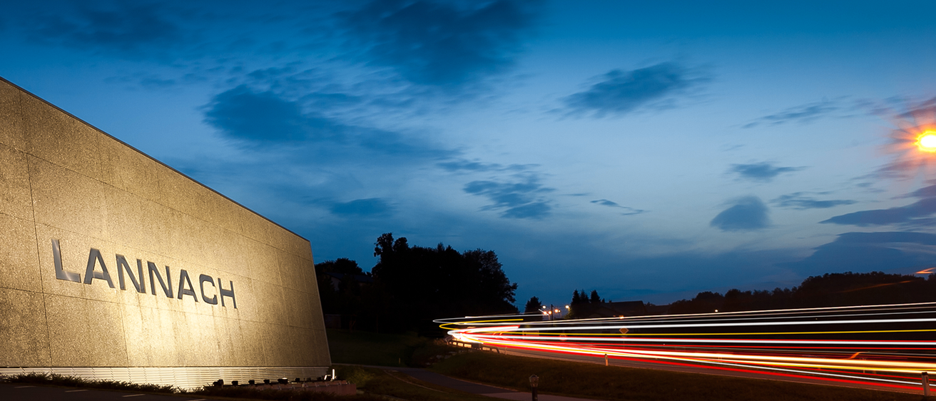 Ein Werbeschild ist in der Dämmerung beleuchtet, der Himmel ist blau mit einigen Wolken, und Autos erzeugen lange Lichtspuren auf der Straße.