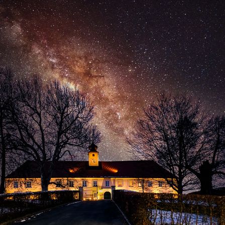 Ein Haus mit einem Glockenturm und einem Pfad davor, unter einem Sternenhimmel. Bäume auf beiden Seiten des Weges.
