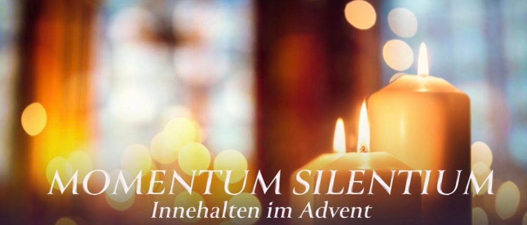 Zwei brennende Kerzen mit warmem Schein, vor einem verschwommenen Hintergrund mit dem Text 'Momentum Silentium'.