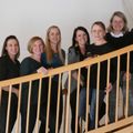 Eine Gruppe von Frauen posiert für ein Foto, während sie auf der Treppe mit weißen Geländern stehen und lächelnd nach vorne schauen.