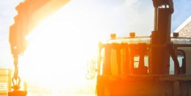 Ein Kran ist auf einem Lastwagen positioniert, mit der Sonne, die hell dahinter scheint und eine warme Atmosphäre auf die Szene wirft.