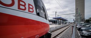 Ein BB-Zug nähert sich einem Bahnhof unter einem bewölkten Himmel. Die Vorderseite des Zuges ist in Rot und Weiß gehalten. Der Bahnhof hat ein blaues Vordach und ein Schild mit der Aufschrift 'Golis'.