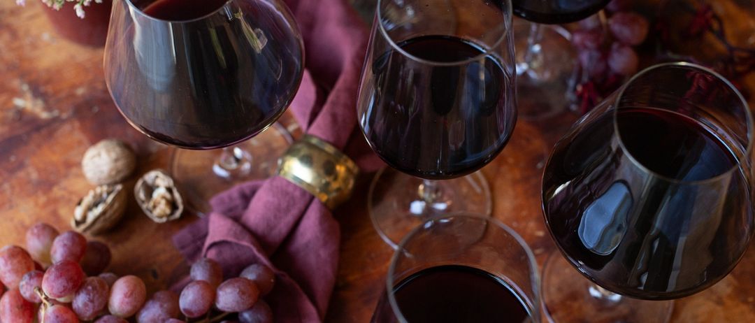 Ein Holztisch mit mehreren Weinglasern, gefüllt mit dunklem Wein, Trauben, Feigen und Walnüssen.