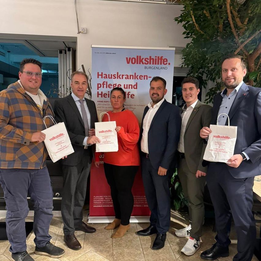 Fünf Personen stehen vor einem Banner von Volkshilfe. Eine Frau in der Mitte hält einen weißen Beutel. Sie alle lächeln.