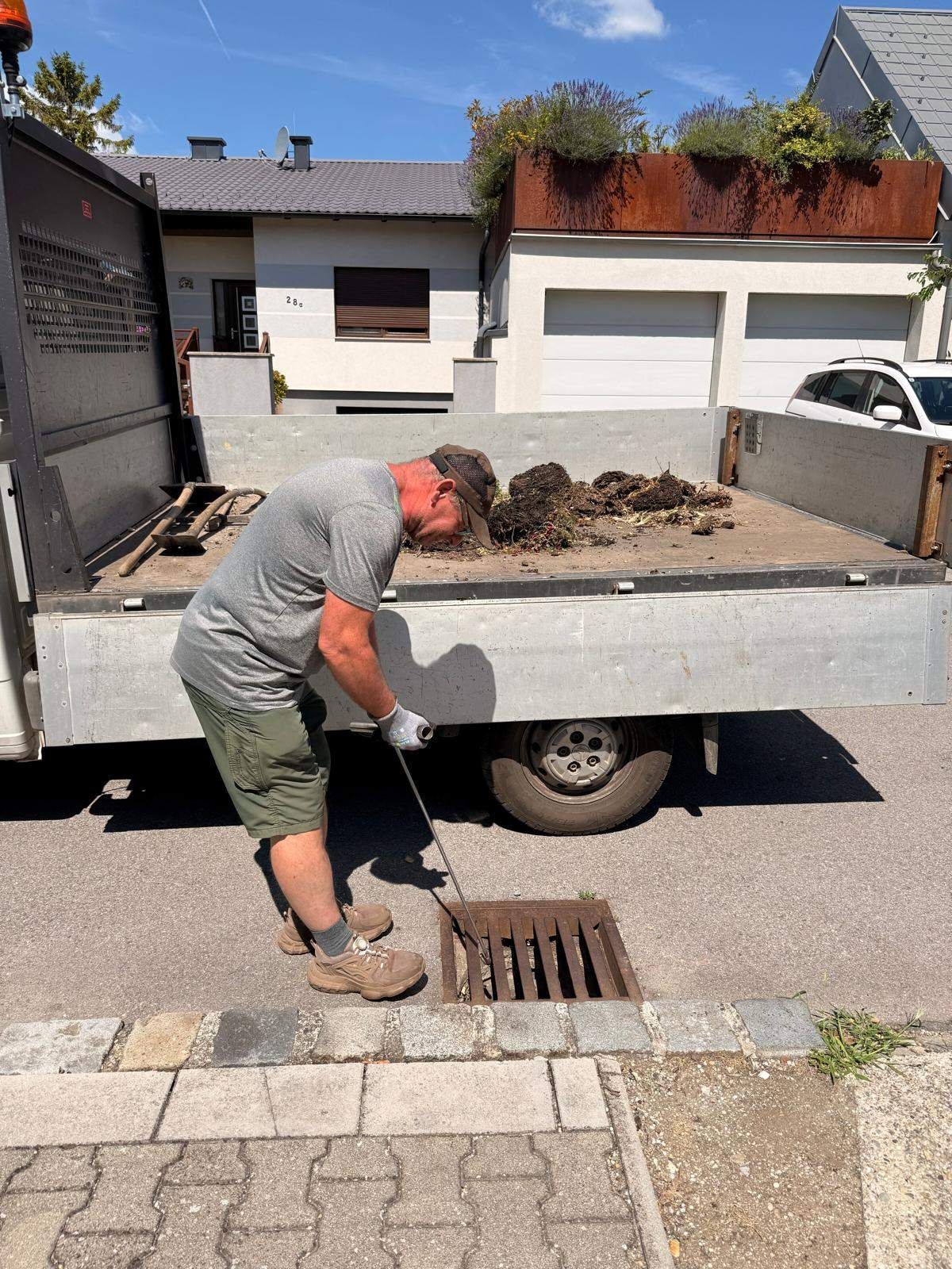 Ein Mann entfernt Schmutz aus einem Lkw am Bordstein mit einer Schaufel. Der Lkw ist vor einem Haus geparkt.