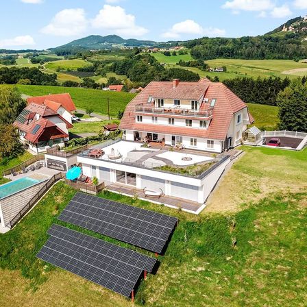 Luftaufnahme eines modernen Hauses mit Solarmodulen, einem Swimmingpool und einer grünen Landschaft.