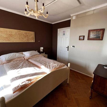 Ein Schlafzimmer mit einem Bett, Kissen und einer Kronleuchter. Es gibt zwei Bilderrahmen an der Wand. Der Raum hat Holzböden.